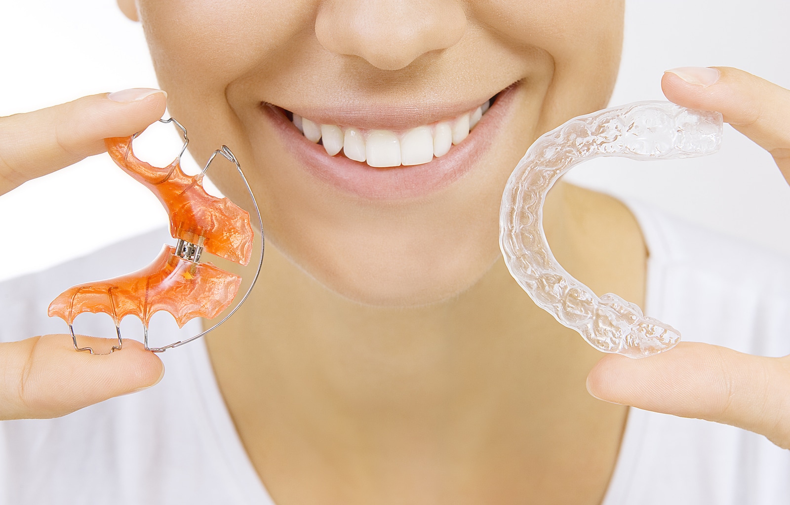 Patient holding a clear and Hawley retainer, showing retainers wearing braces