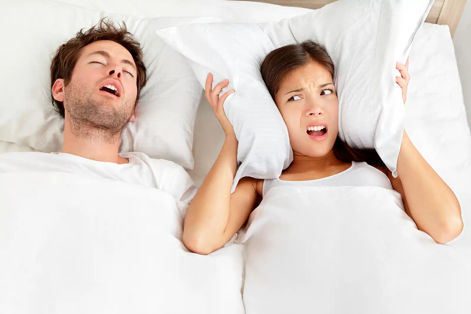 Woman covering ears while partner snores, illustrating snoring treatment with oral sleep devices