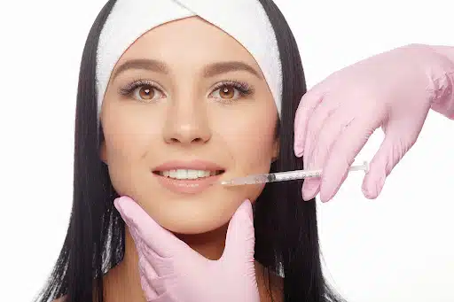 Woman receiving lip filler injections for natural lip enhancement by a cosmetologist wearing pink gloves